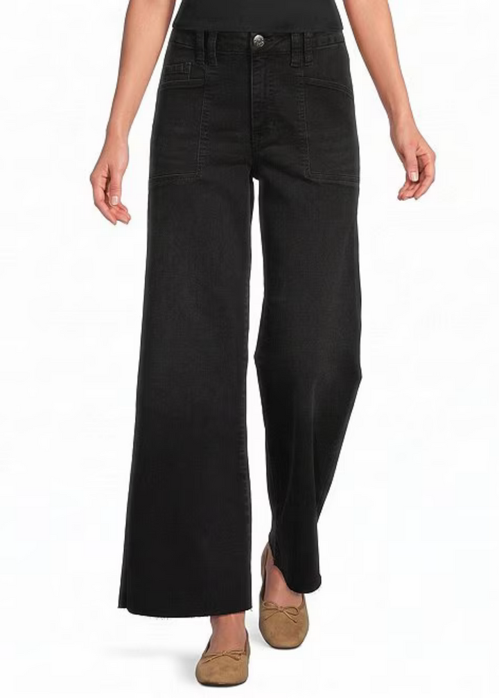 A model wearing a pair of wide-leg black jeans with a button fly and brown flat shoes, shown from the waist down on a white background.