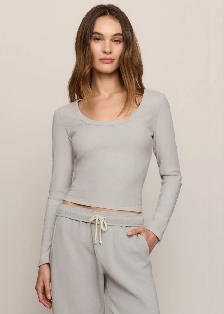 A woman modeling a light gray long-sleeve crop top and matching gray sweatpants against a plain beige studio background.