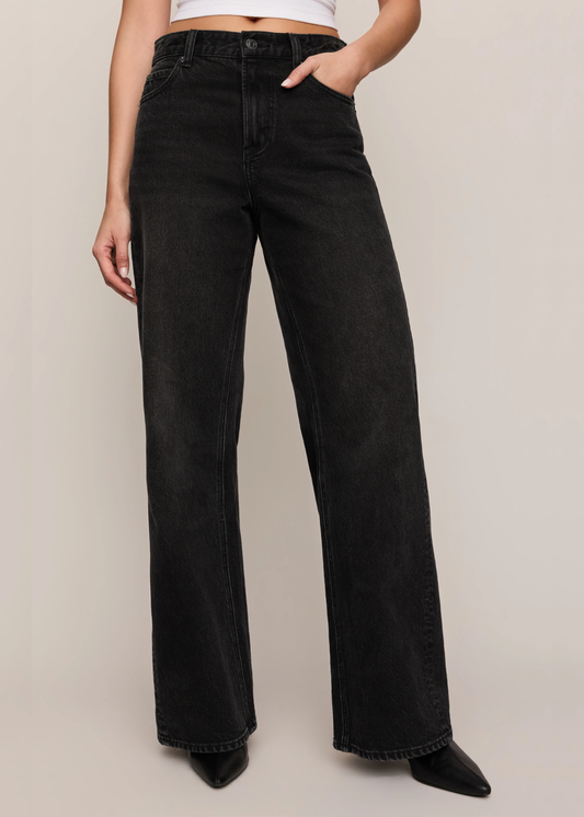 Model wearing black denim with a black boot and hand in the pocket. 