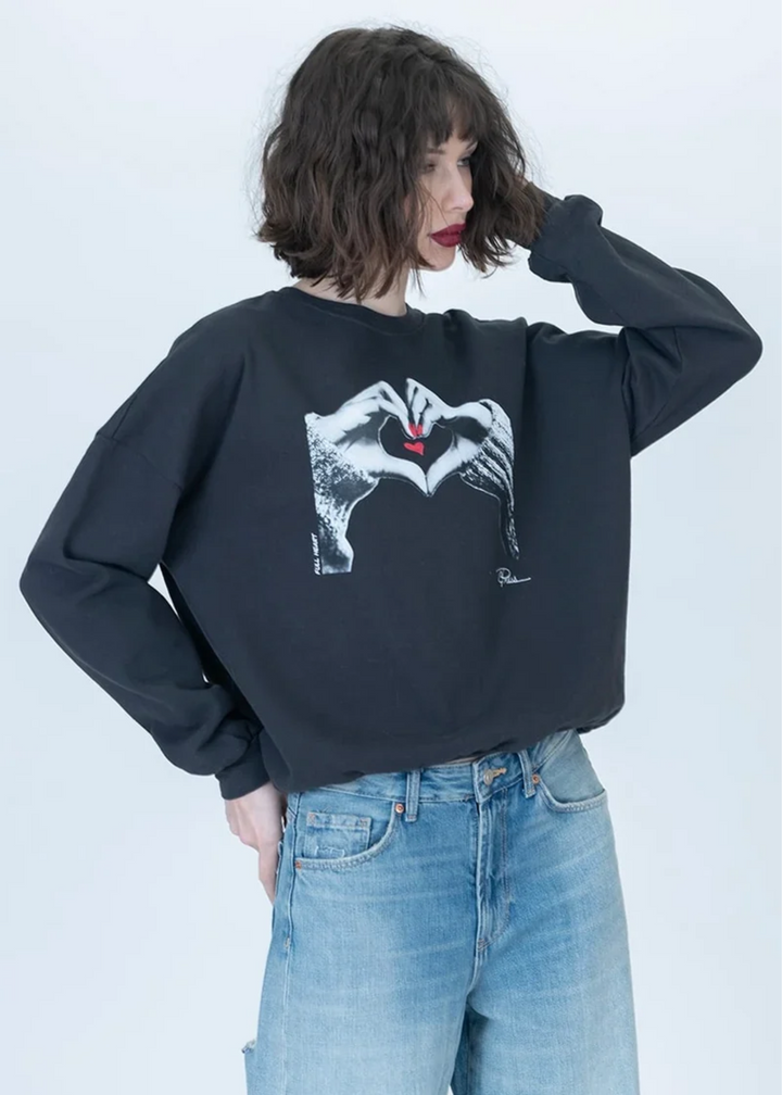 Woman wearing a grey sweatshirt with heart hands on it.
