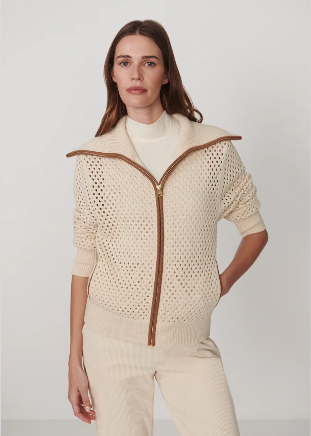 Woman wearing a beige knit cardigan with a zipper on a white background