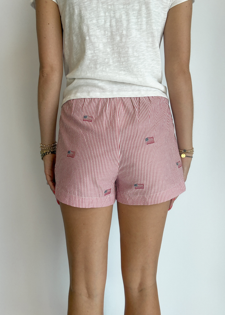 Woman turned around wearing red and white striped shorts with embroidered American flags on them with a white t-shirt