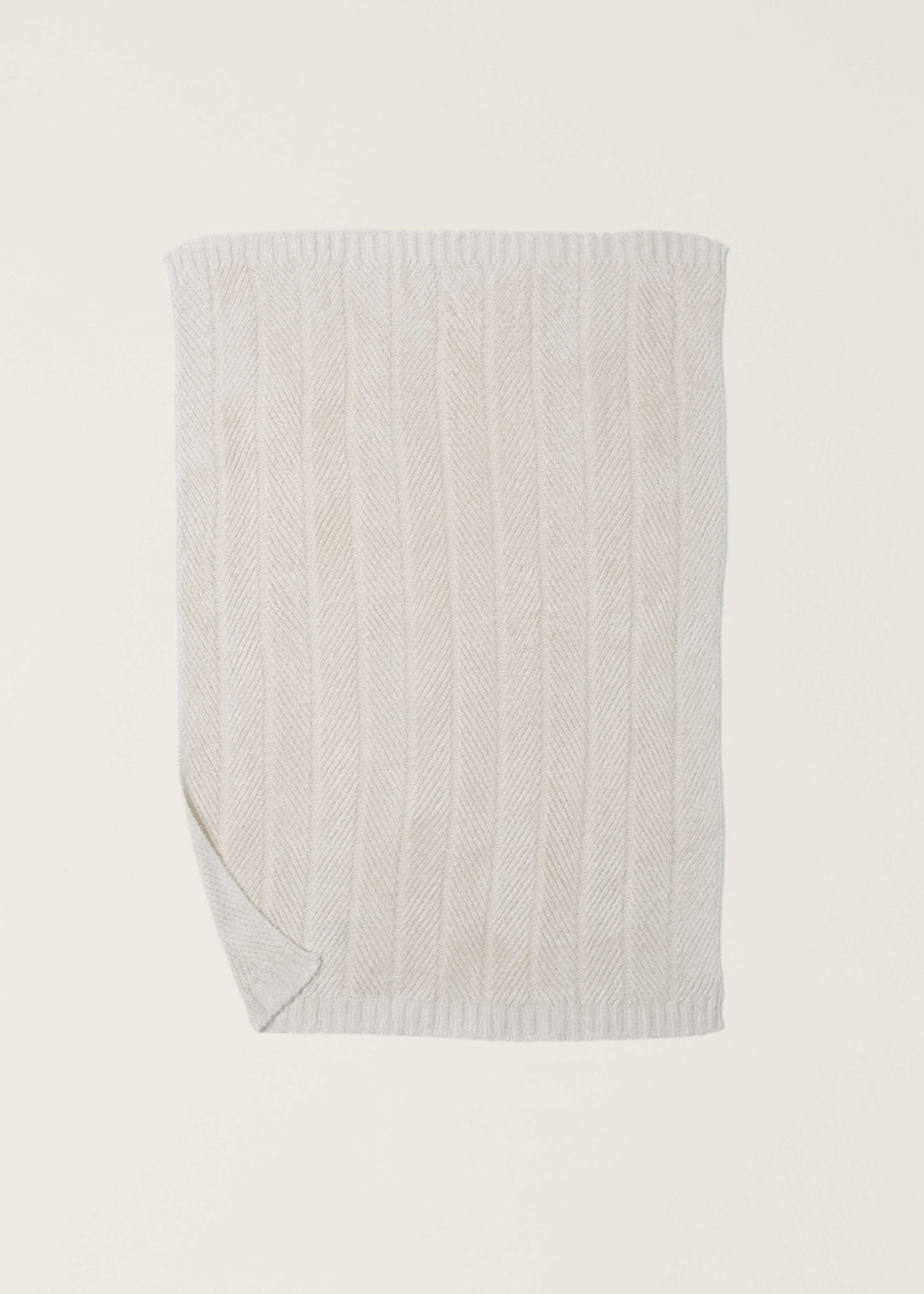 Cream blanket with a herringbone pattern and the bottom left corner folded laid on a white background