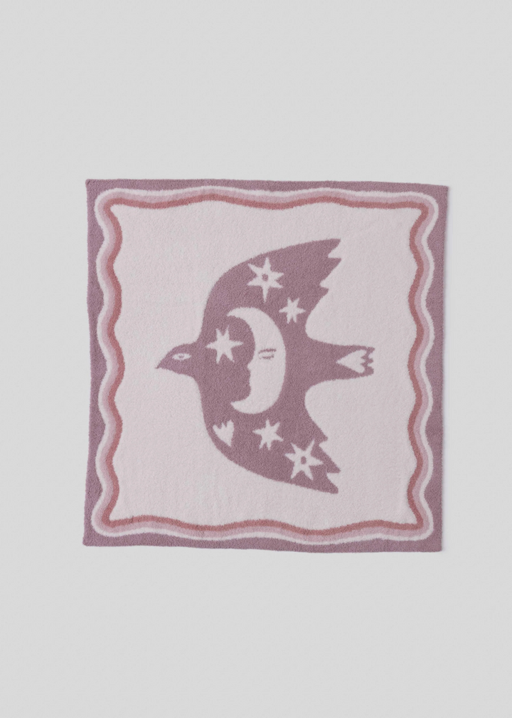 A pink blanket with a white center with a desert bird and moon graphic with wavy pink trim on a white background