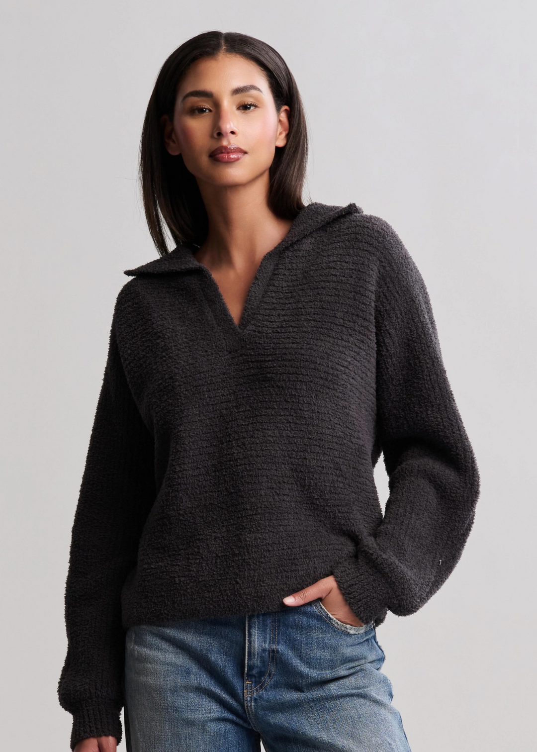 Woman wearing a black collared pullover with jeans in front of a white background