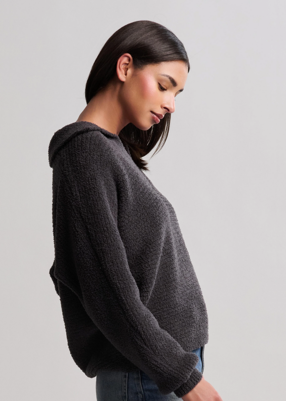 Woman turned to the side wearing a black collared pullover with jeans in front of a white background