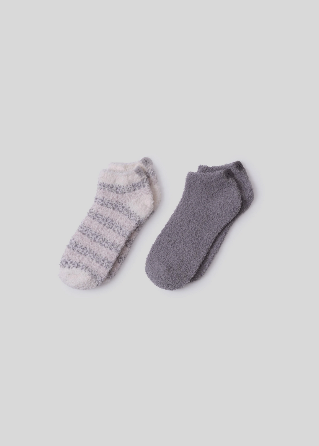 A pair of grey and white striped socks laying beside a pair of grey sock laying on a white background