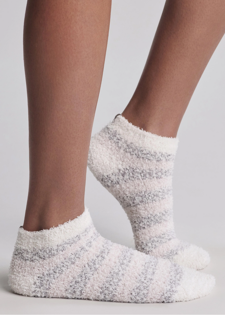 Close up of a woman wearing grey and white striped ankle socks standing in front of a white background