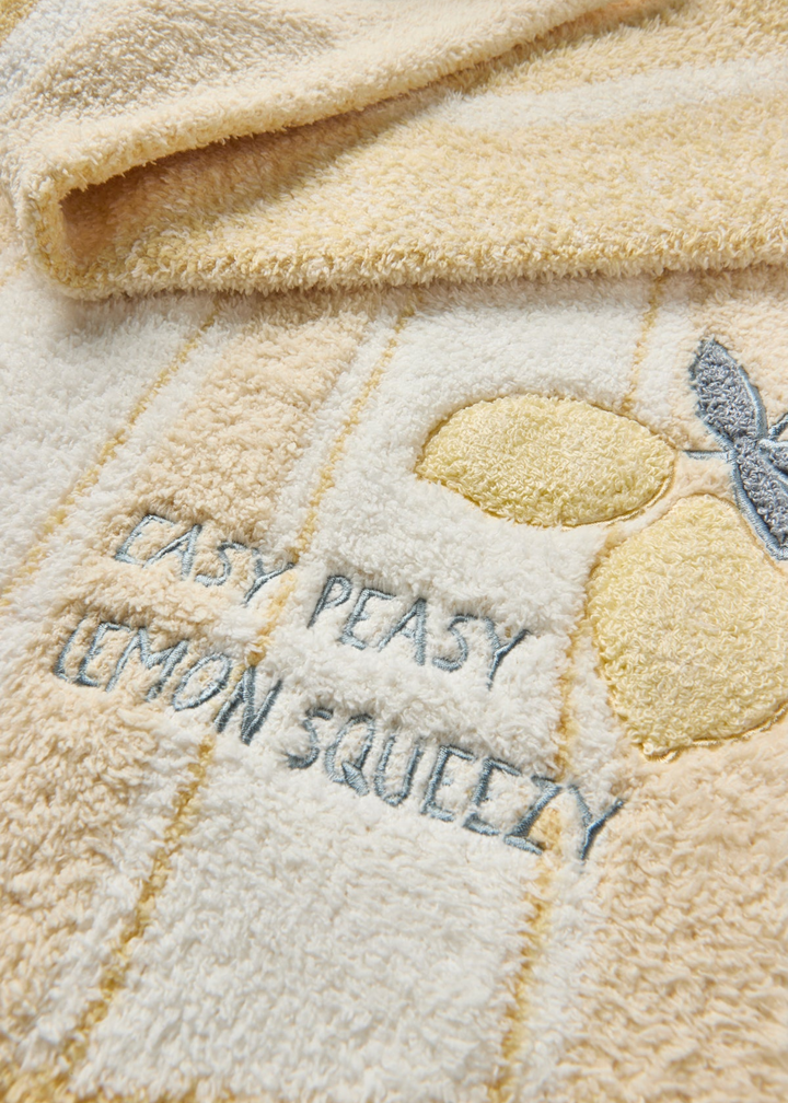Close up of a yellow baby blanket with a striped pattern and lemon embroidery and "EASY PEASY LEMON SQUEEZY" lettering
