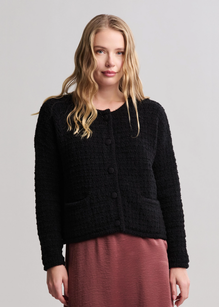 Woman wearing a textured button front black cardigan with a mauve skirt standing in front of a white background