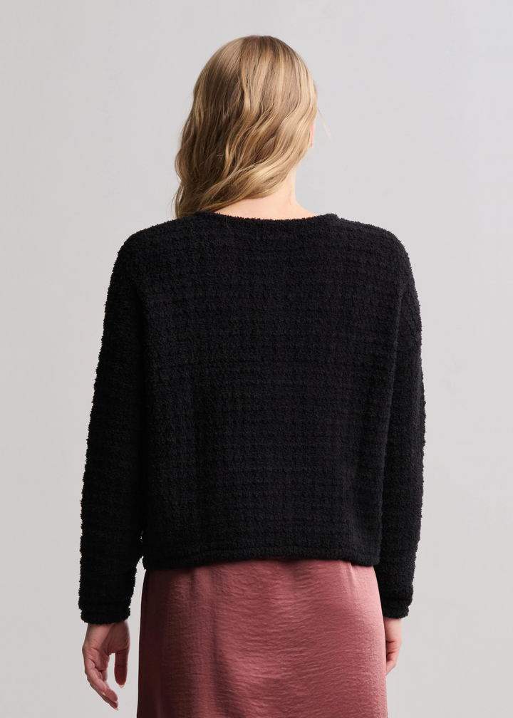 Woman turned around wearing a textured button front black cardigan with a pink skirt standing in front of a white background