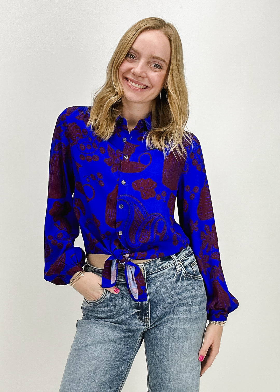 A woman wearing a bright blue and maroon printed button-up long-sleeve top by FRNCH Paris, styled with light-wash jeans, perfect for a chic and vibrant casual look.