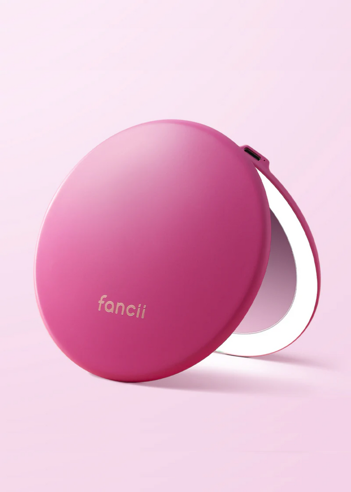 Pink round compact mirror with a built in LED light on a light pink background