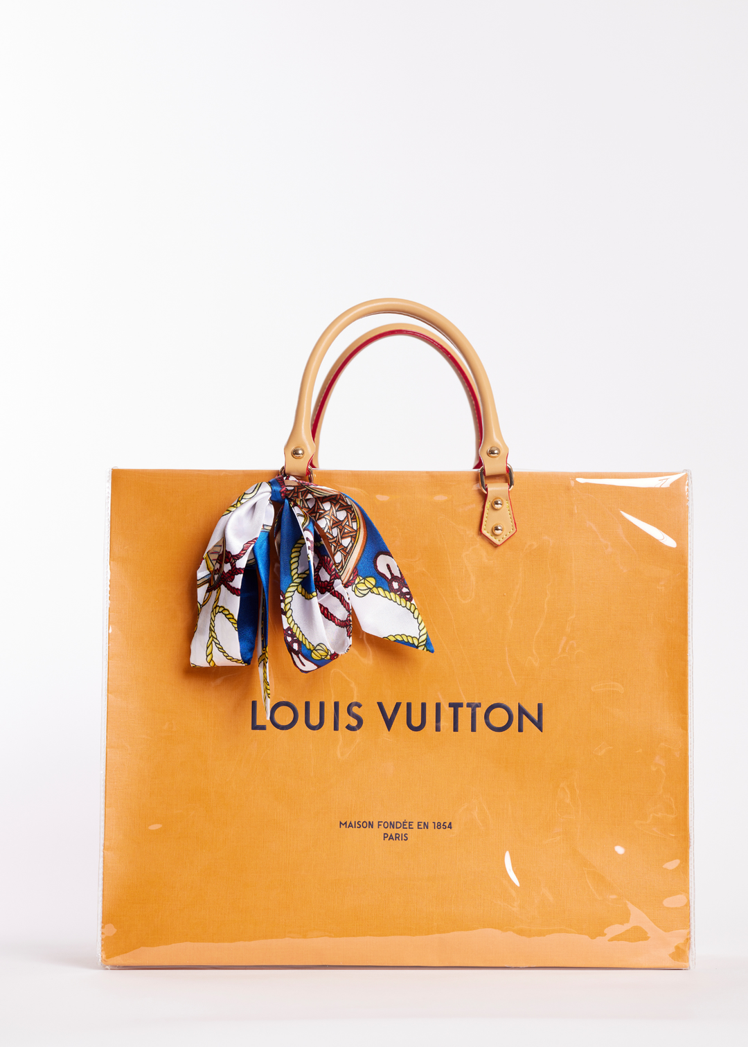Clear coated orange Louis Vuitton shopping bag with a scarf tied on the handle