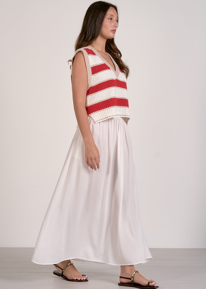 Woman turned to the side wearing a red and white striped sweater vest and a white skirt