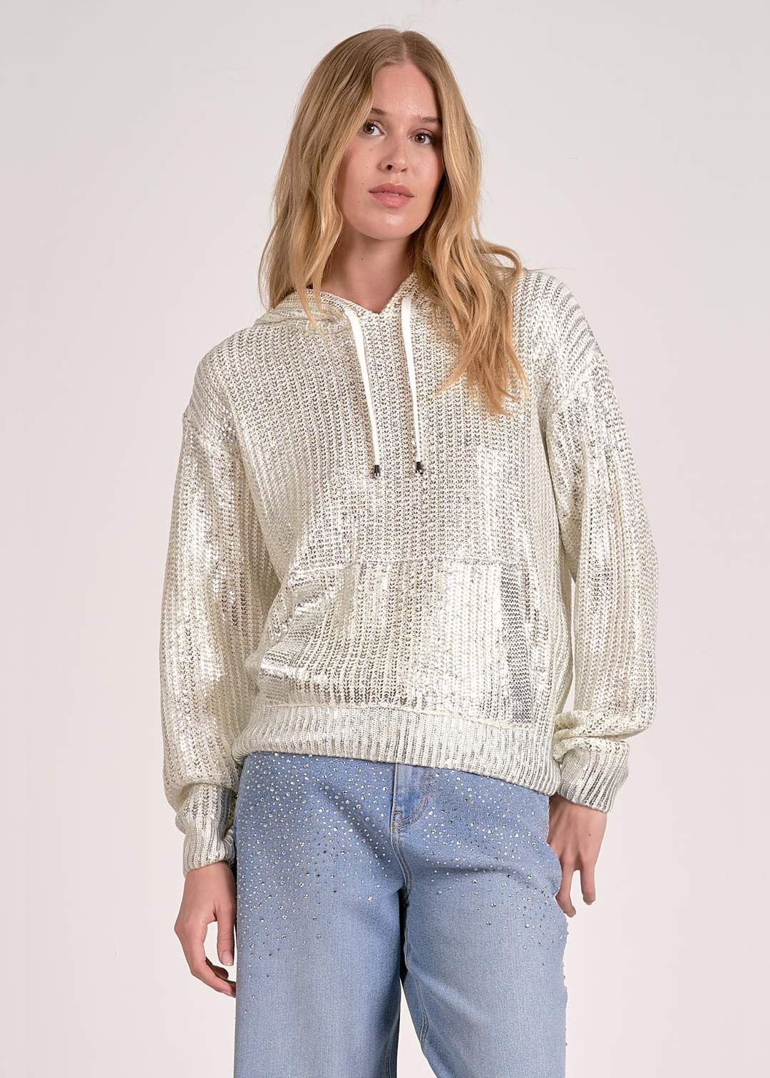 Woman wearing a white sequin hoodie with jeans against a white background