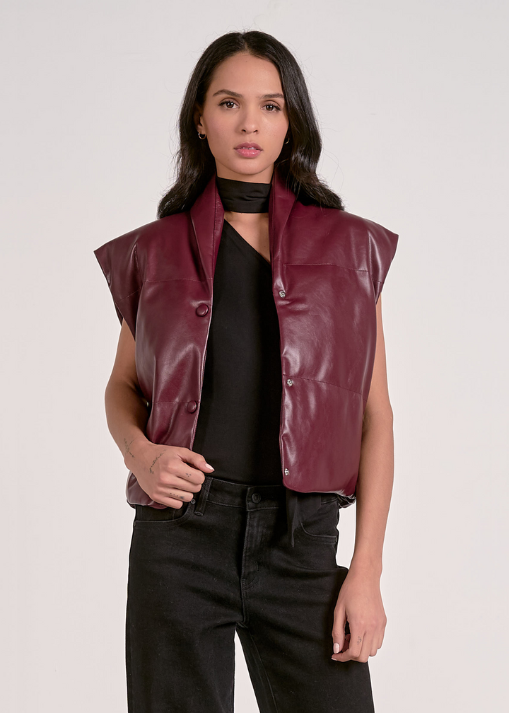 Woman wearing a plum colored leather vest in front of a grey background