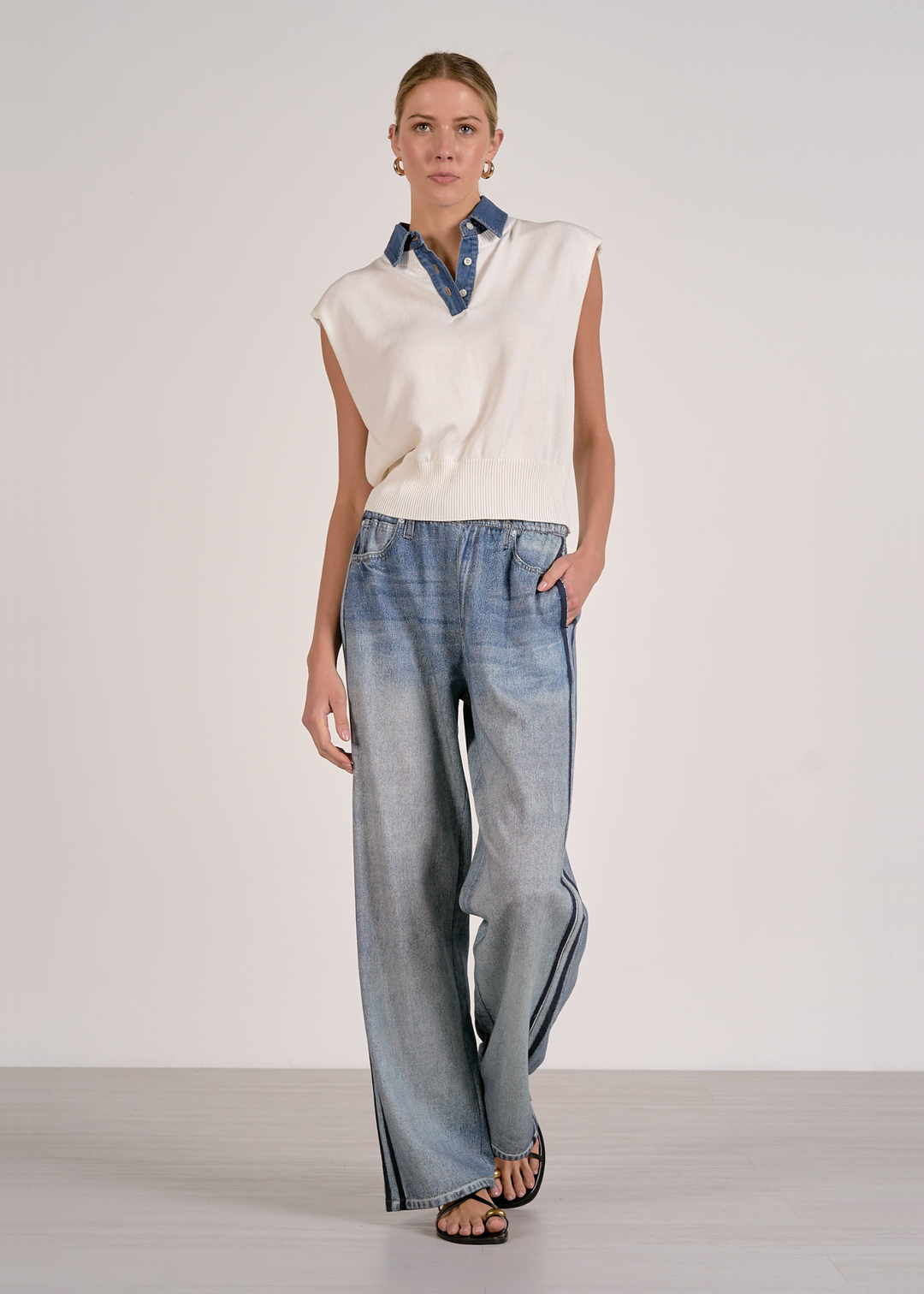 Woman with hand in pocket wearing a white knit top with jeans 