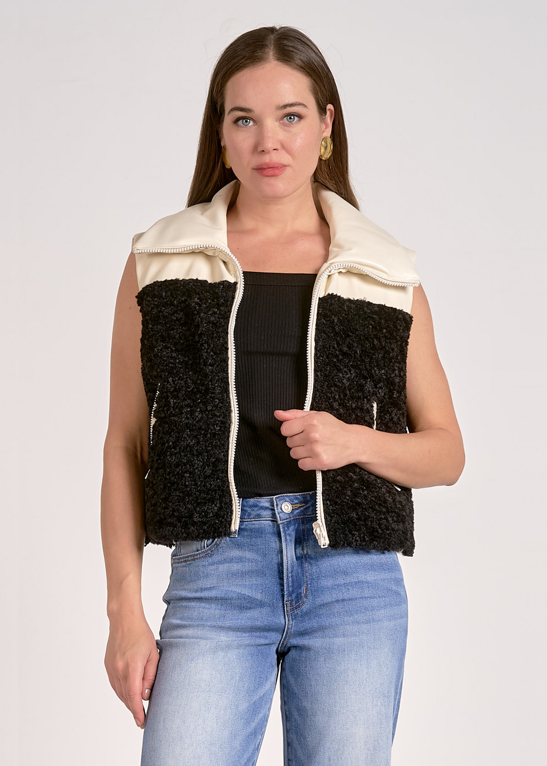 Woman wearing a black and white fuzzy vest with a large collared neckline in front of a grey background