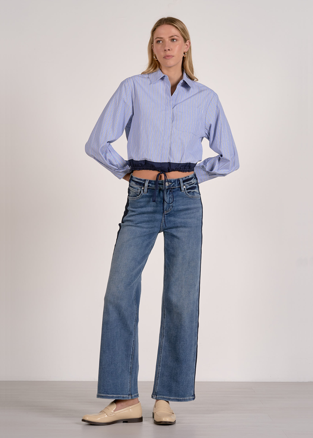 Woman wearing a blue stripe button down with a navy cinched waistline and jeans