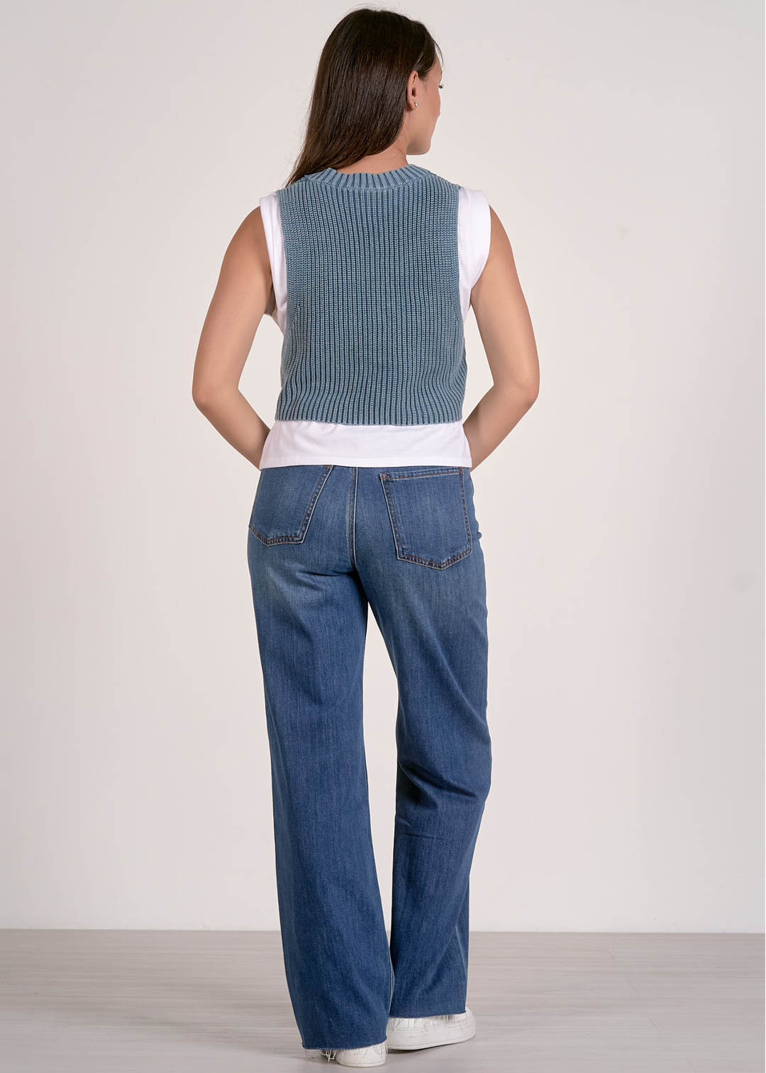 Woman turned around wearing a blue and white layered top with jeans