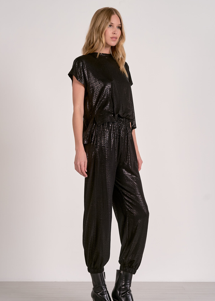 Woman wearing a shiny black short sleeve jumpsuit against a grey wall