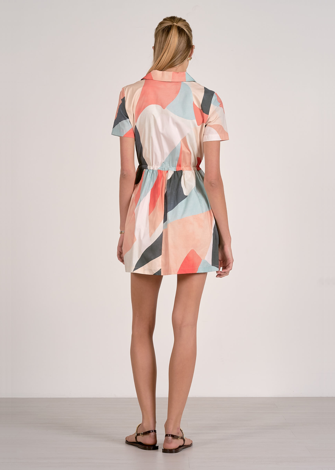 Woman turned around wearing a short sleeve mini dress with a collared neckline and a pastel print pattern