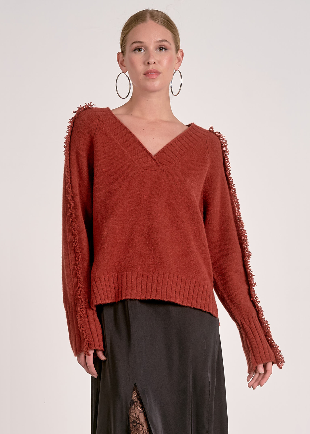 Woman wearing a v-neck rust colored sweater against a white background