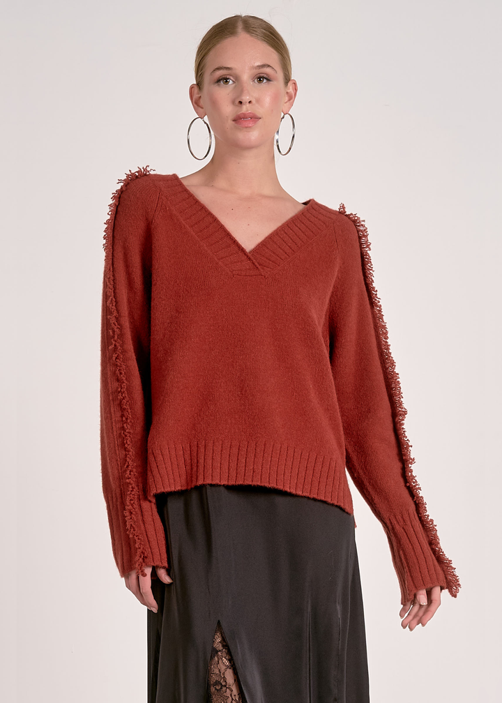 Woman wearing a v-neck rust colored sweater against a white background