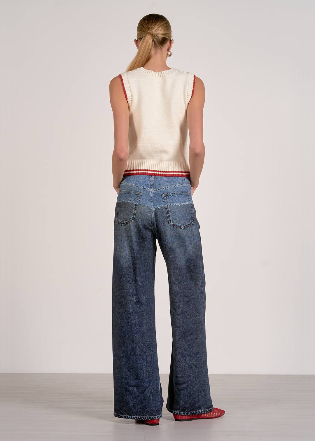 Woman turned around wearing a white sleeveless knit top with red striped trim and jeans