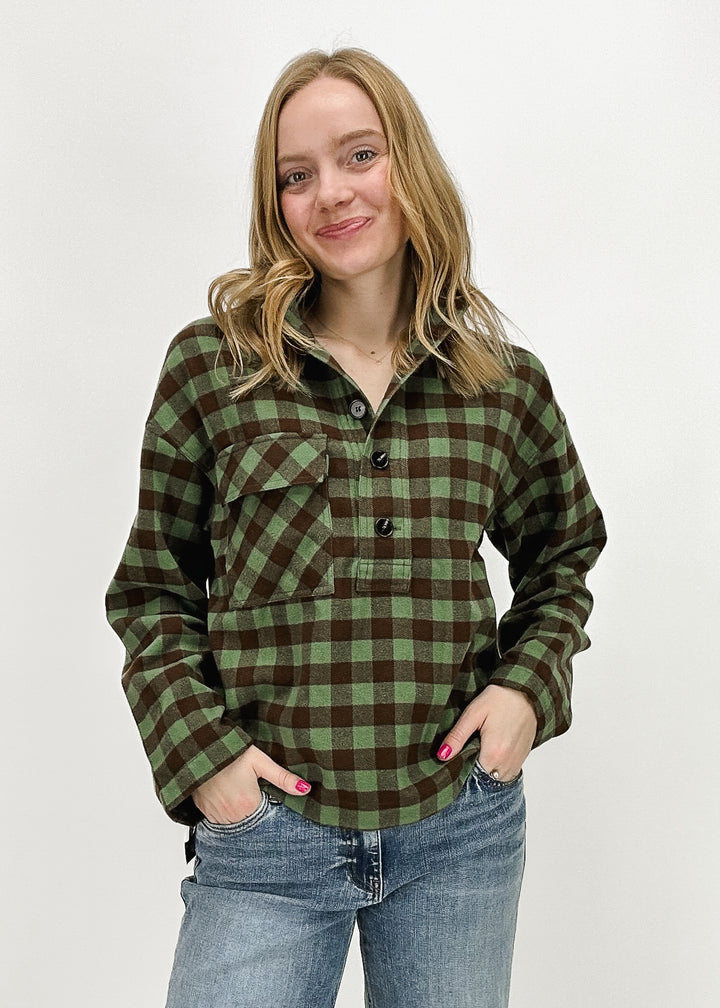 A woman wearing a green and brown plaid checkered long-sleeve pullover shirt by FRNCH Paris, styled with light-wash jeans, perfect for cozy fall or winter fashion.