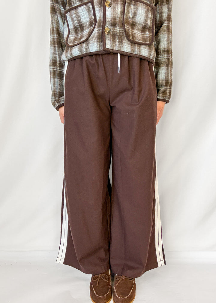 Woman wearing brown wide leg pants with white stripe down the side