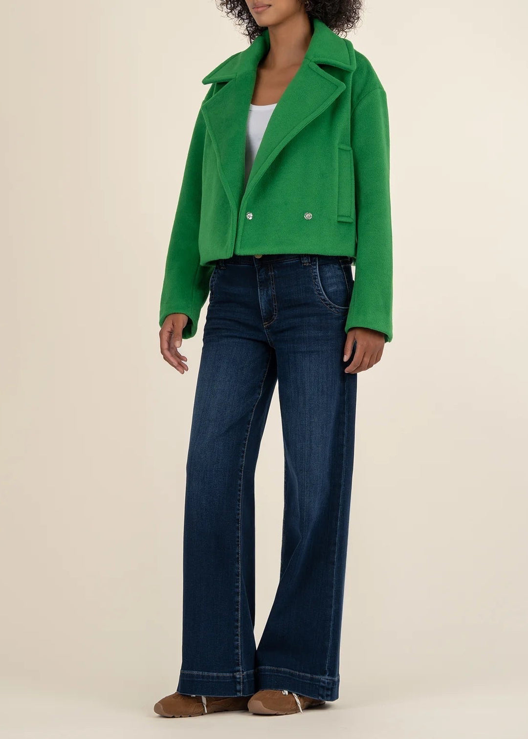 Person wearing a green jacket and blue jeans on a beige background