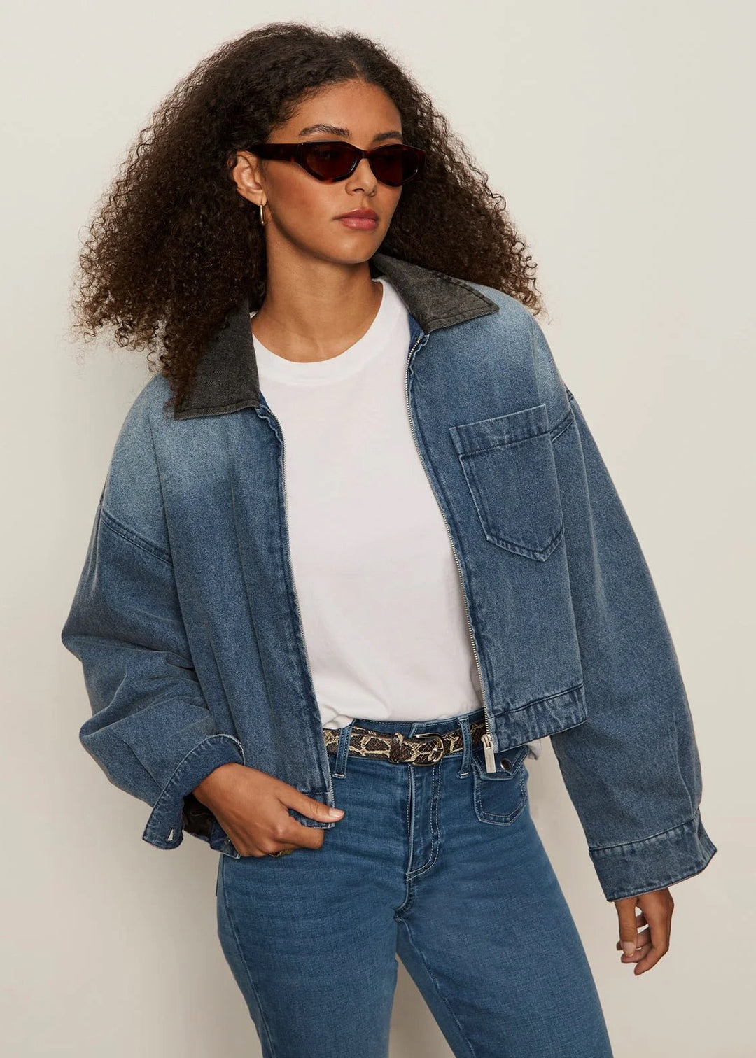 Woman wearing a denim jacket and jeans with a plain background