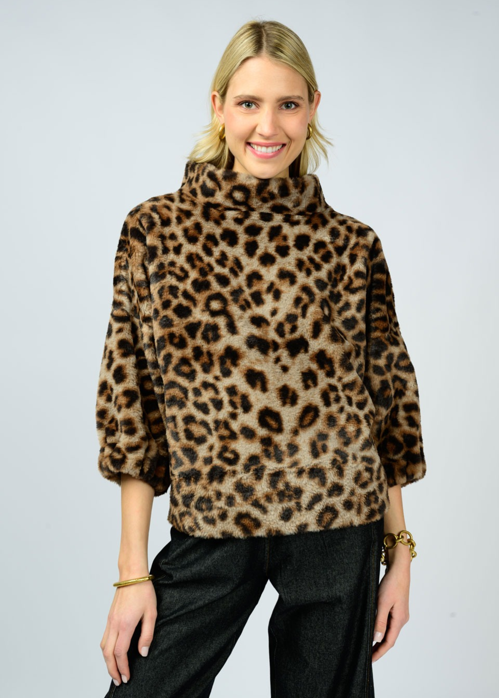 Woman wearing a leopard print sweater with a mock neckline and 3/4 length sleeves and black pants in front of a white background