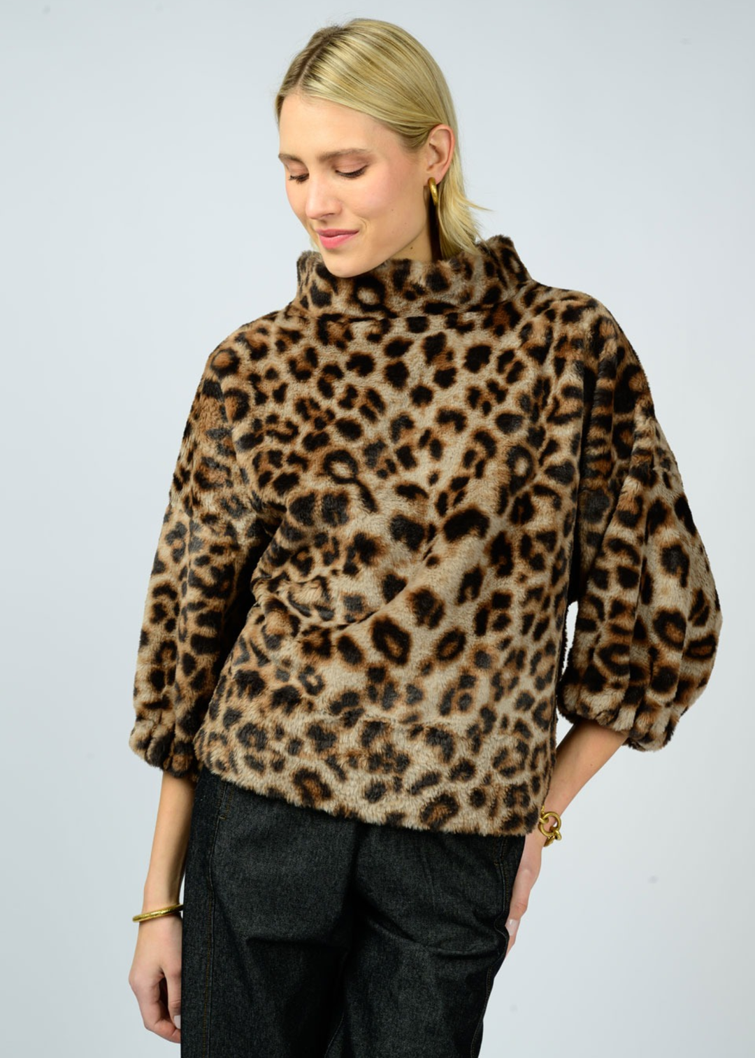 Woman with hand on hip wearing a leopard print sweater with a mock neckline and 3/4 length sleeves and black pants in front of a white background