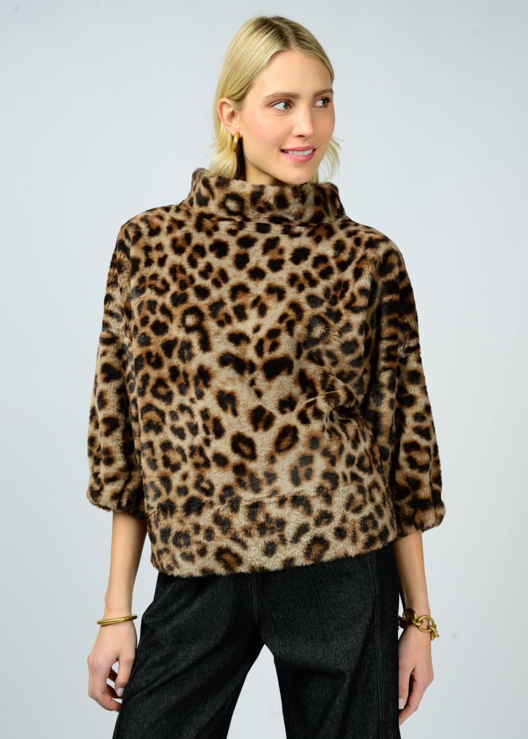 Woman wearing a leopard print sweater with a mock neckline and 3/4 length sleeves and black pants in front of a white background