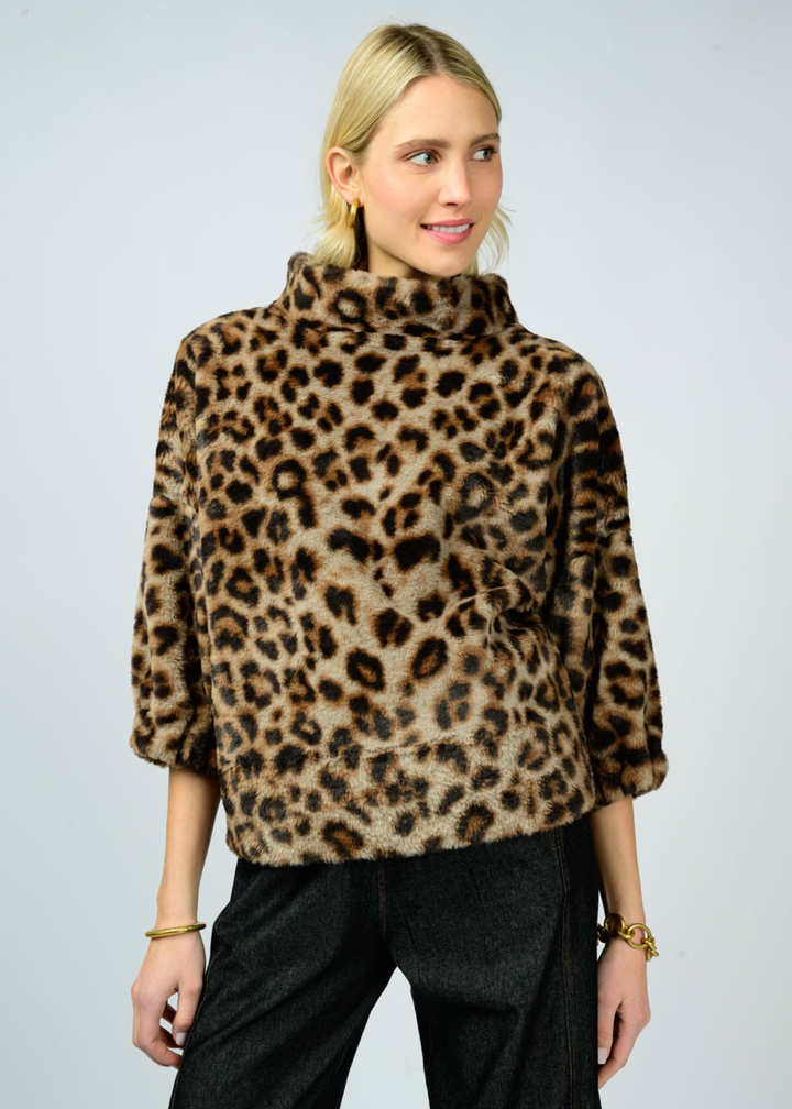 Woman wearing a leopard print sweater with a mock neckline and 3/4 length sleeves and black pants in front of a white background