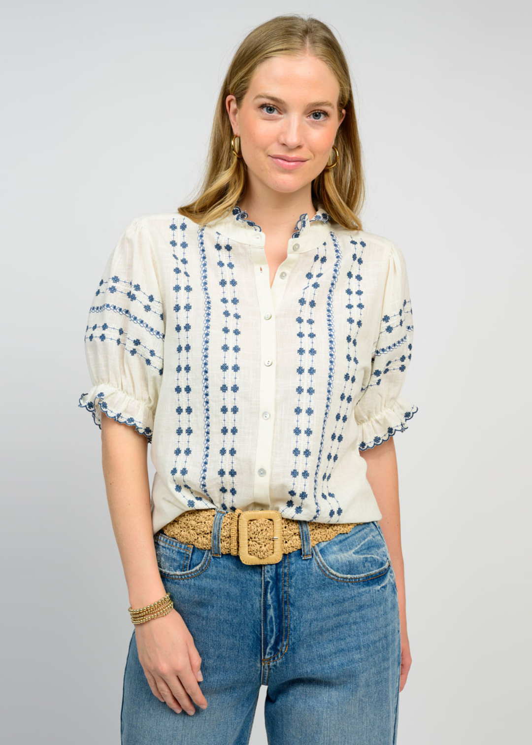 Woman wearing an ivory puff sleeve top with blue embroidery and jeans