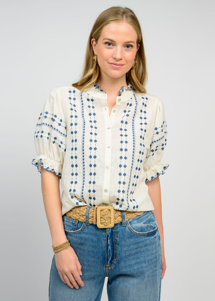 Woman wearing an ivory puff sleeve top with blue embroidery and jeans