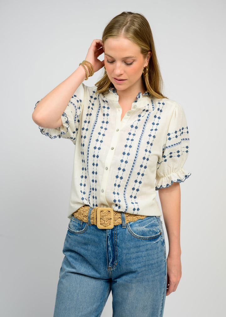 Woman wearing an ivory puff sleeve top with blue embroidery and jeans