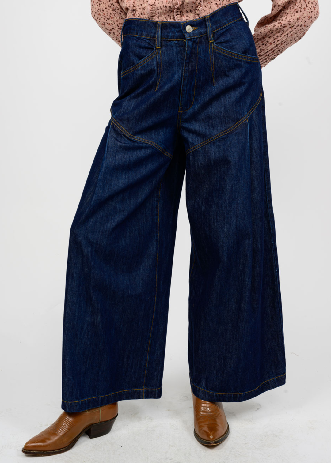 Woman wearing dark blue wide leg jeans with brown boots in front of a white background