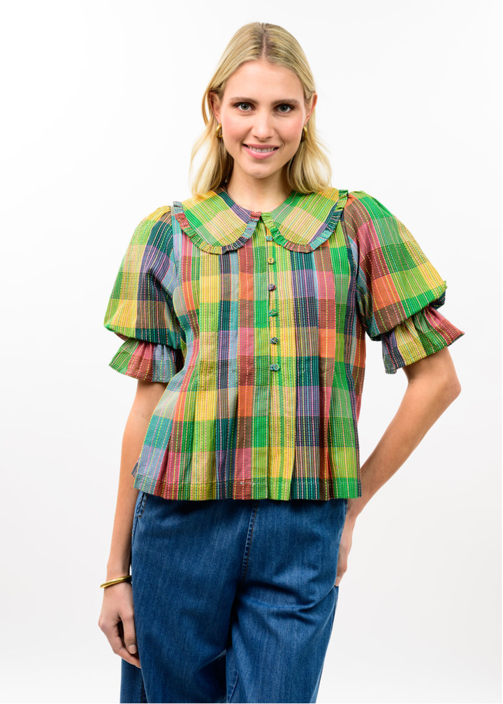 Woman wearing a multicolor plaid top with dark blue jeans against a white background