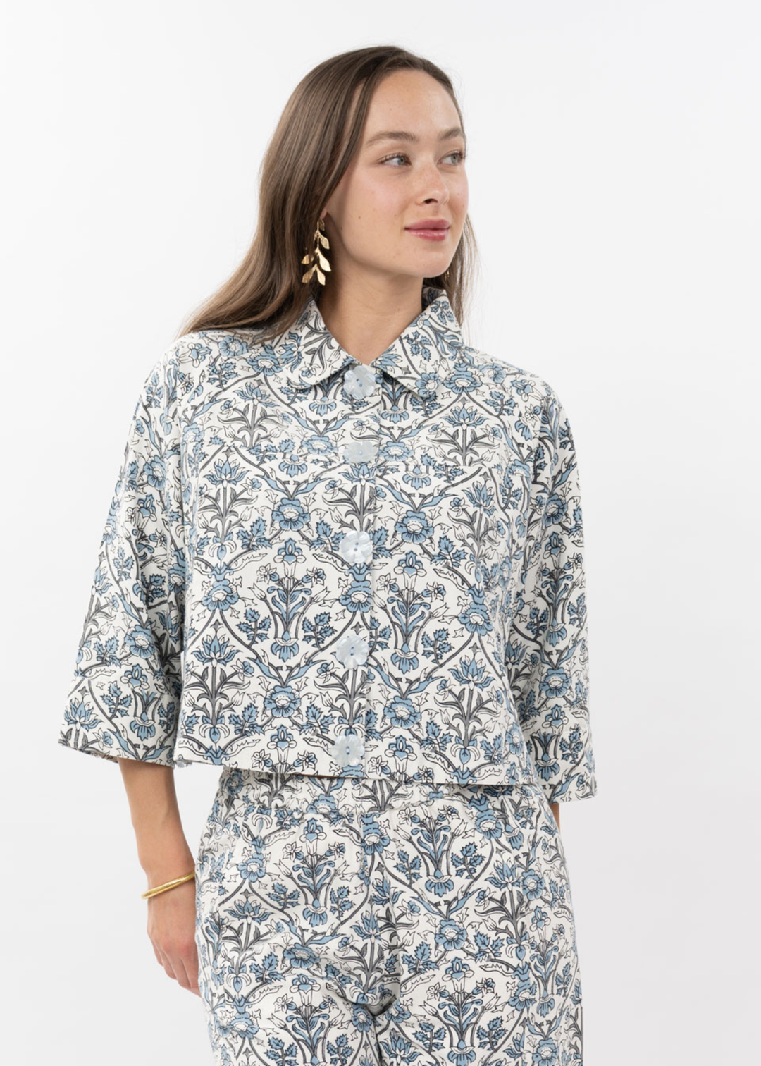 Woman wearing a blue and white floral button down top with 3/4 length sleeves and matching pants