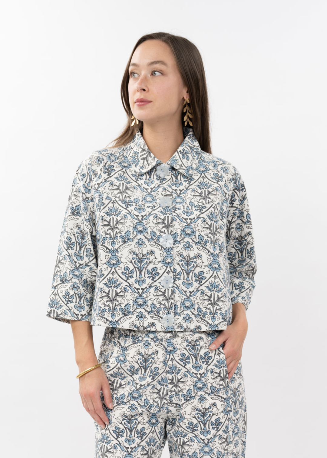 Woman wearing a blue and white floral button down top with 3/4 length sleeves and matching pants