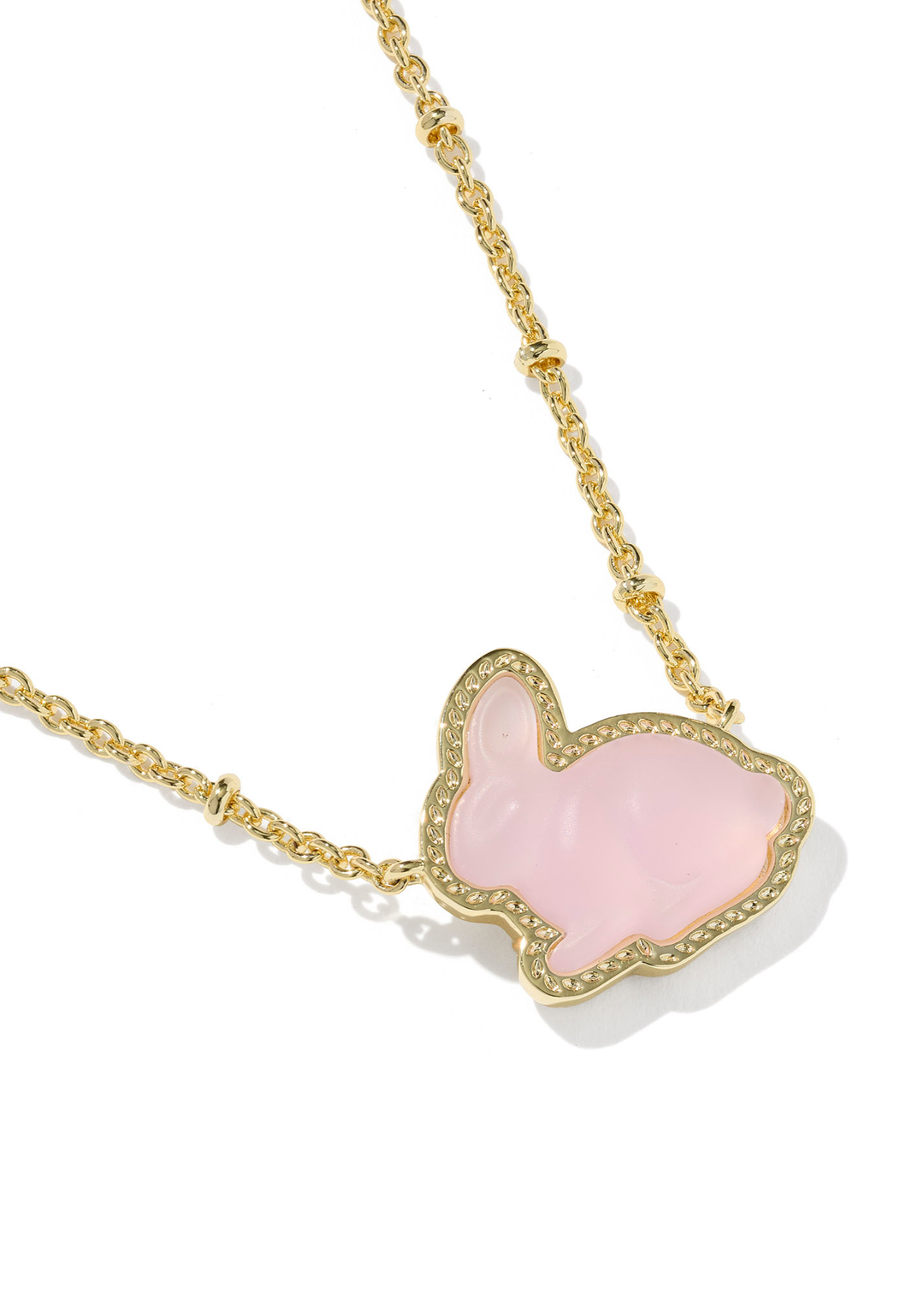 Close up of a pink bunny pendant necklace with a gold chain on a white background