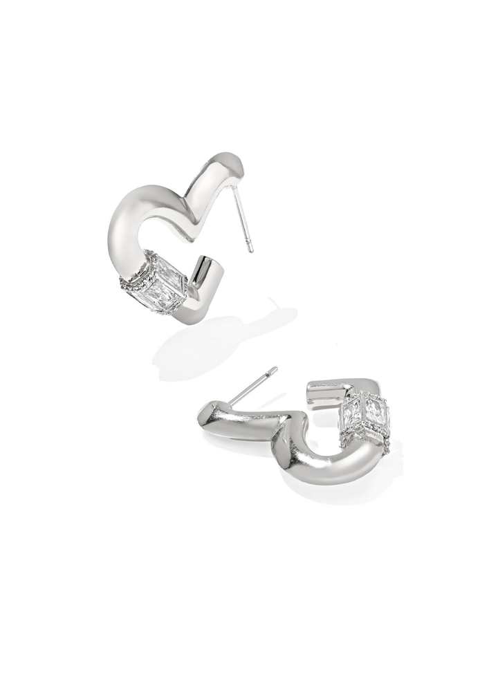 A pair of rhodium heart shaped hoop earrings with CZ details laying on a white background
