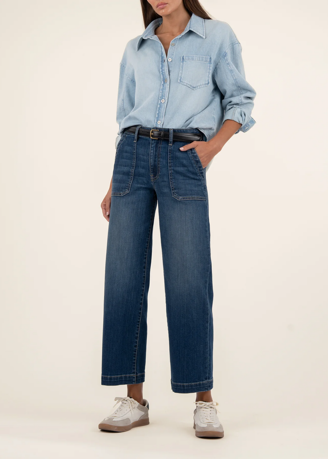Woman wearing dark denim wide leg, high rise jeans with a light denim button down in front of a white background