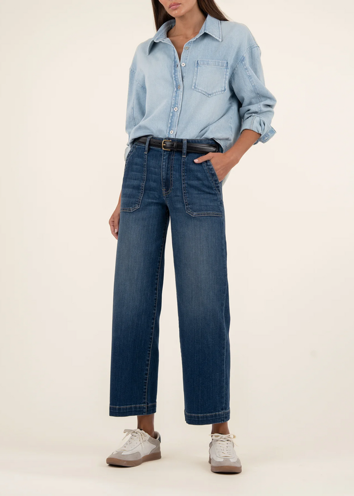 Woman wearing dark denim wide leg, high rise jeans with a light denim button down in front of a white background