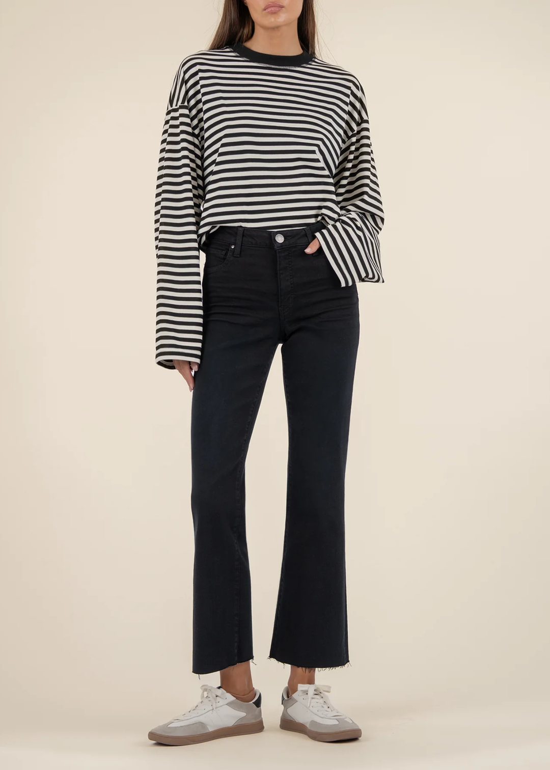 Woman wearing black jeans with a black and white striped sweater and white sneakers standing in front of a white background